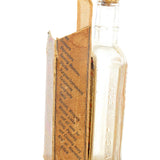 Clear glass bottle with a book-shaped label on a white background