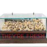 Display case with glass top containing pebbles and a sign saying 'THEY'RE FRESH' on a white background