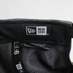 Close-up of a New Era cap with brand logo and tag on a light gray background