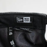 Close-up of a New Era cap with brand logo and tag on a light gray background