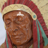 Carved wooden head of a Native American figure with headdress on a plain background