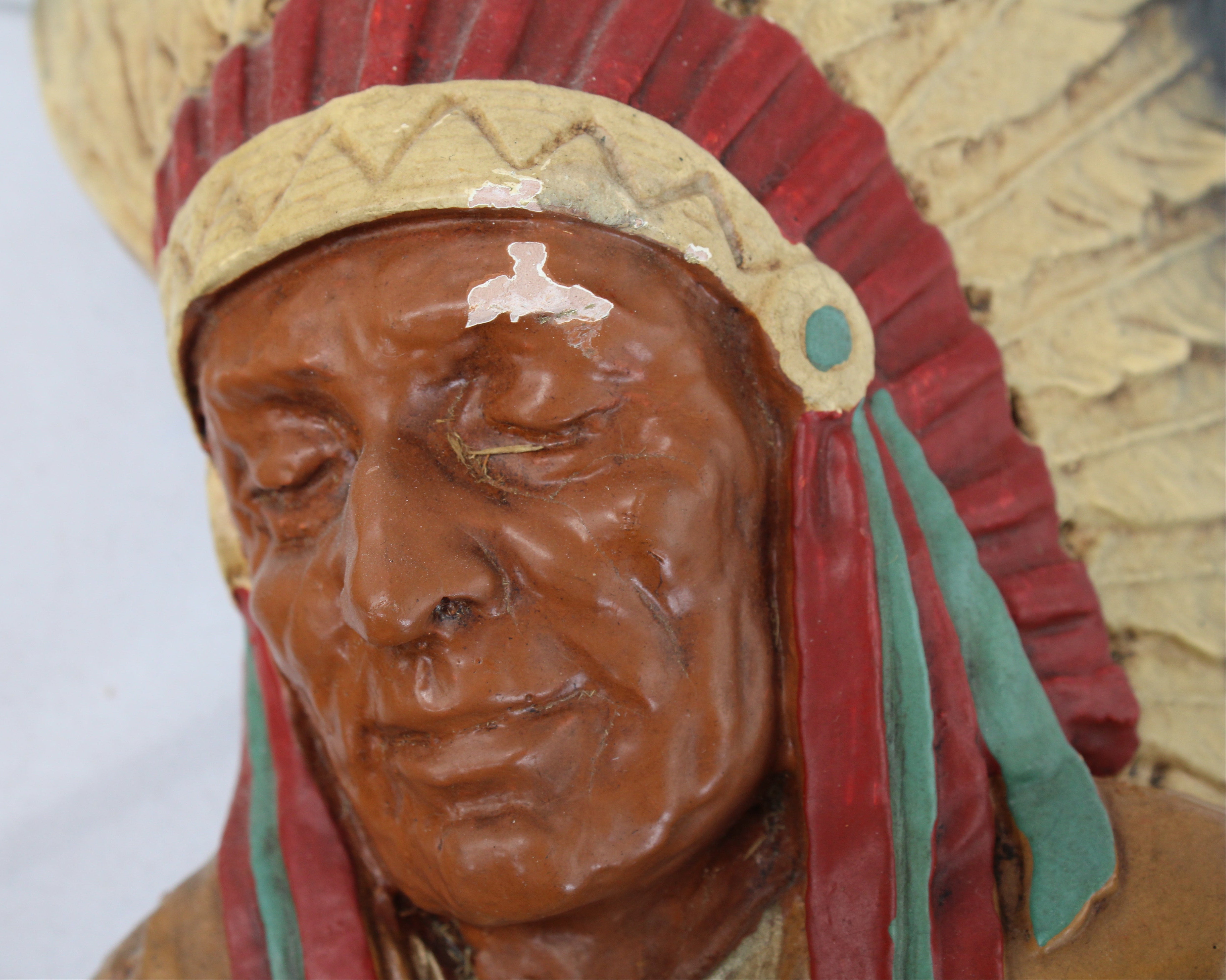 Carved wooden head of a Native American figure with headdress on a plain background