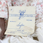 Doll in a floral dress holding a 'Daddy's Long Legs' tag with 'Sofie' written on it.