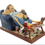Statue of a person lounging on a couch with food and drinks, on a white background