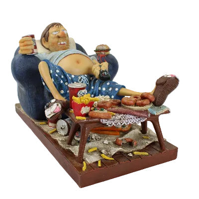 Decorative figurine of a person lounging on a chair with food and drinks on a table.