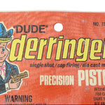 Vintage packaging of a 'Dude' derringer precision pistol with cartoon illustration on an orange background.