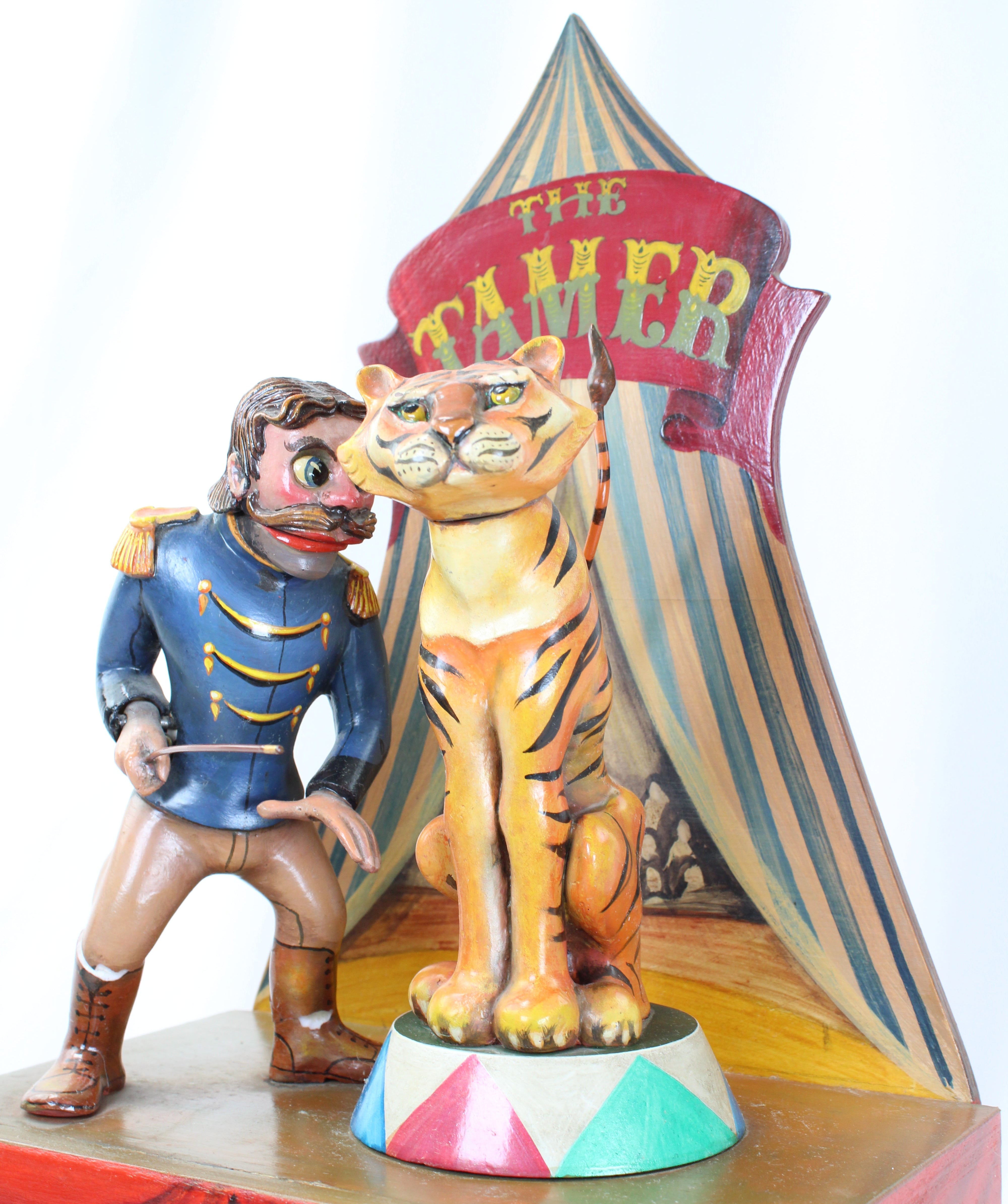 Carnival ride figure with a tiger and a ringmaster in front of a striped tent.