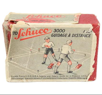 Vintage Schuco toy packaging with illustration of two figures and text on a white background
