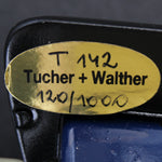 Close-up of a gold label on a black and blue object with 'Tucher + Walther' branding.