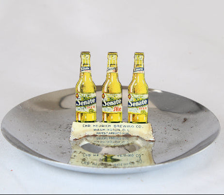 Three Senate Ale bottles on a metallic tray with a white background