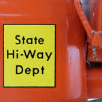 Close-up of a yellow 'State Hi-Way Dept' label on an orange background