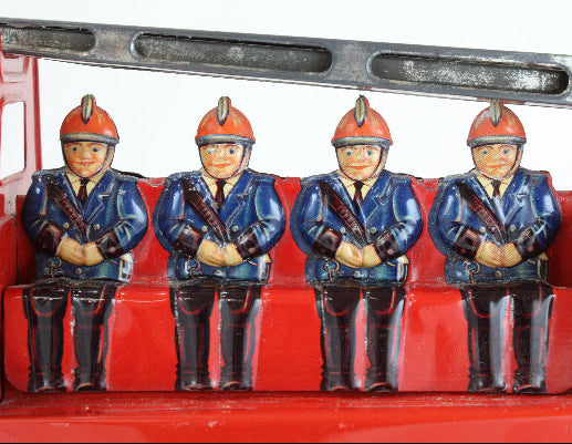 Four toy firemen figures sitting on a red fire truck toy.