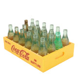 Yellow Coca-Cola crate filled with vintage miniature glass bottles on a white background