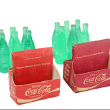 Set of green Coca-Cola miniature bottles and red cardboard holders on a white background
