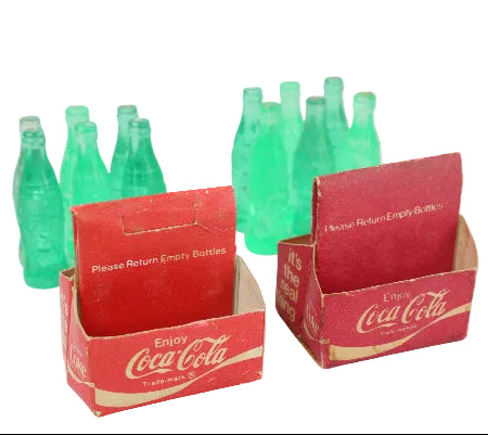 Set of green Coca-Cola miniature bottles and red cardboard holders on a white background