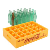 Yellow Coca-Cola miniature bottle crate with green glass bottles on a white background