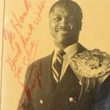Vintage photograph of boxer Joe Frazier with a championship belt and signature on a yellowed background