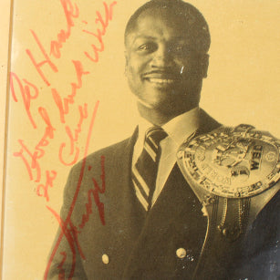 Vintage photograph of boxer Joe Frazier with a championship belt and signature on a yellowed background