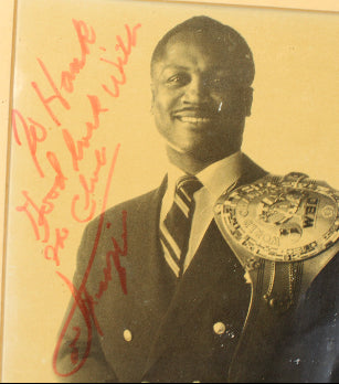 Vintage photograph of boxer Joe Frazier with a championship belt and signature on a yellowed background