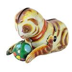 Vintage wind-up cat toy with a striped yellow, brown, and cream body, wearing an orange collar and interacting with a colorful green ball, set against a plain white background.