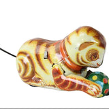 Vintage wind-up cat toy with a striped yellow, brown, and orange body, wearing an orange collar and interacting with a green polka-dot ball, photographed on a white background.