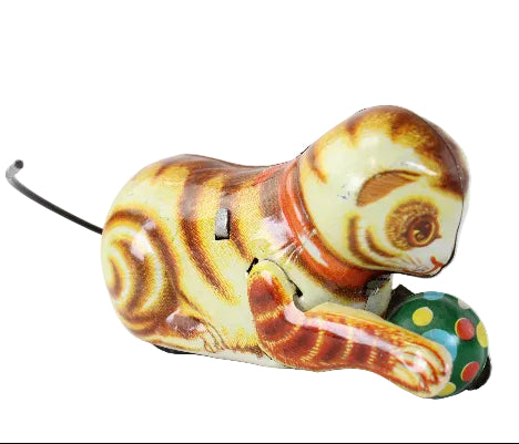 Vintage wind-up cat toy with a striped yellow, brown, and orange body, wearing an orange collar and interacting with a green polka-dot ball, photographed on a white background.