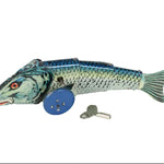 A vintage metal tin fish toy with blue wheels and a small metal key, photographed on a plain white background.
