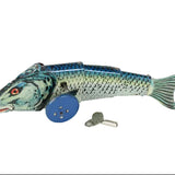 A vintage metal tin fish toy with blue wheels and a small metal key, photographed on a plain white background.