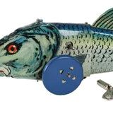 A vintage metal tin fish toy, likely a mackerel, featuring painted scales in blue, green, and silver, with a blue button for a wheel and a small metal key.
