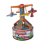 A vintage toy wind-up carousel or spinner with airplane and helicopter details, set against a plain white fabric background.