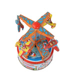 A vintage tin wind-up carousel toy featuring colorful painted details, including blue, orange, red, and yellow, photographed against a plain white background.