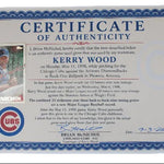 A vintage authenticating certificate for a Kerry Wood Chicago Cubs baseball glove, featuring a blue ornate border, a small inset photo of Kerry Wood in a Cubs uniform, and a UBS logo. A baseball card is tucked into the bottom left corner of the certificate, all displayed on a light gray background.