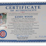 A vintage authenticating certificate for a Kerry Wood Chicago Cubs baseball glove, featuring a blue ornate border, a small inset photo of Kerry Wood in a Cubs uniform, and a UBS logo. A baseball card is tucked into the bottom left corner of the certificate, all displayed on a light gray background.
