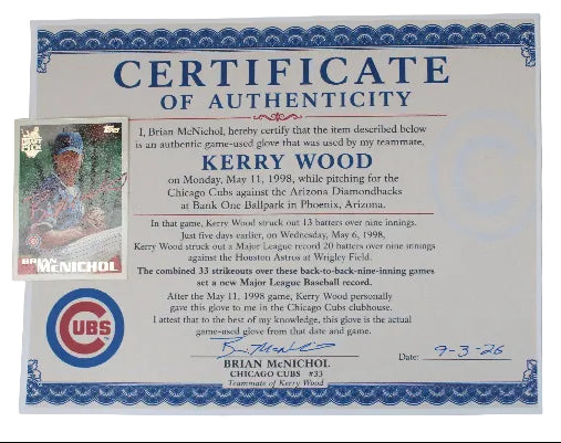 A vintage authenticating certificate for a Kerry Wood Chicago Cubs baseball glove, featuring a blue ornate border, a small inset photo of Kerry Wood in a Cubs uniform, and a UBS logo. A baseball card is tucked into the bottom left corner of the certificate, all displayed on a light gray background.